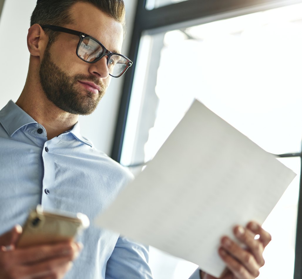 Un uomo consulta un documento con lo smartphone in mano